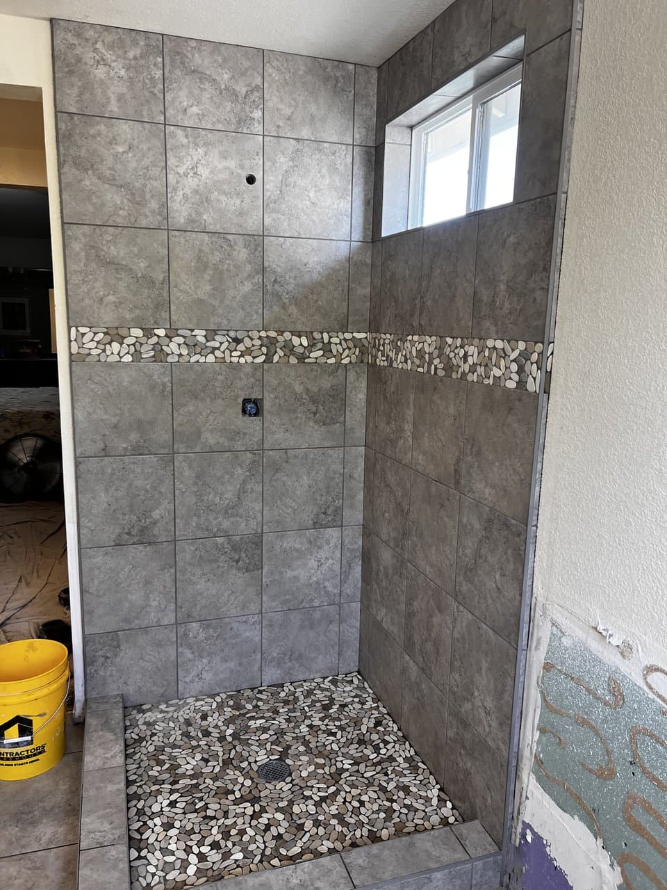Gray tile shower with pebble stone accent band and floor