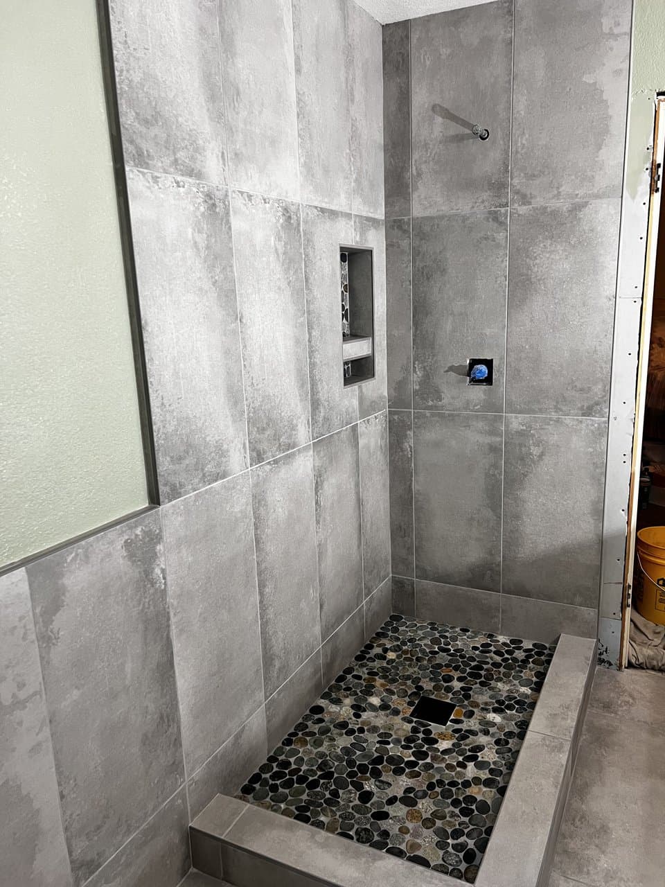Large format gray tile shower with river pebble floor and niche