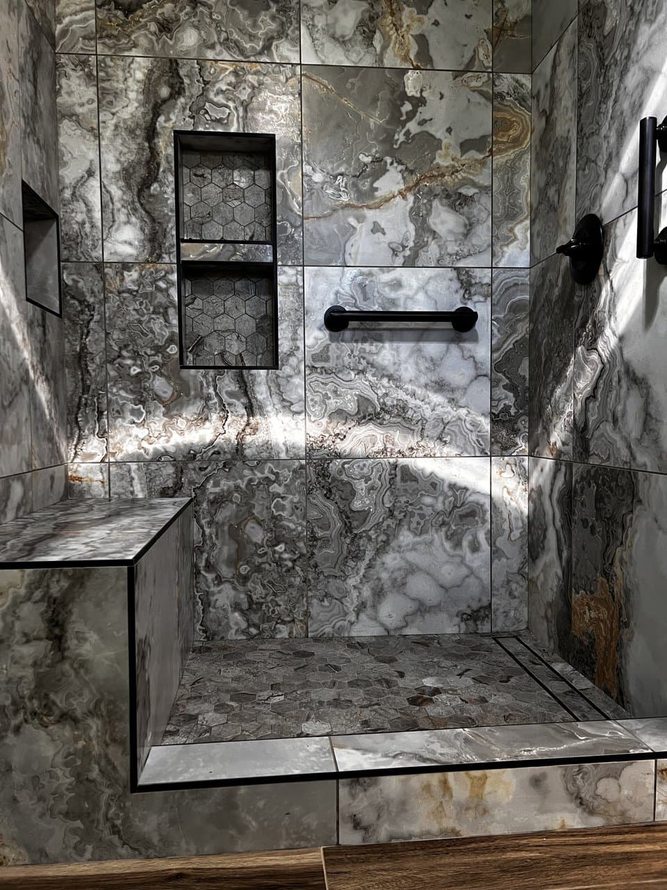 Luxury natural stone shower with custom bench, hexagon niches, and black fixtures