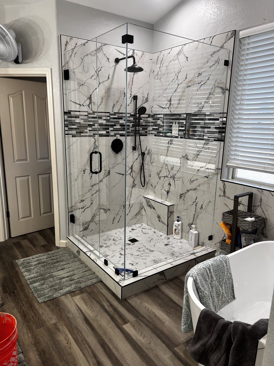 Marble-look tile shower with frameless glass enclosure and mosaic accent band