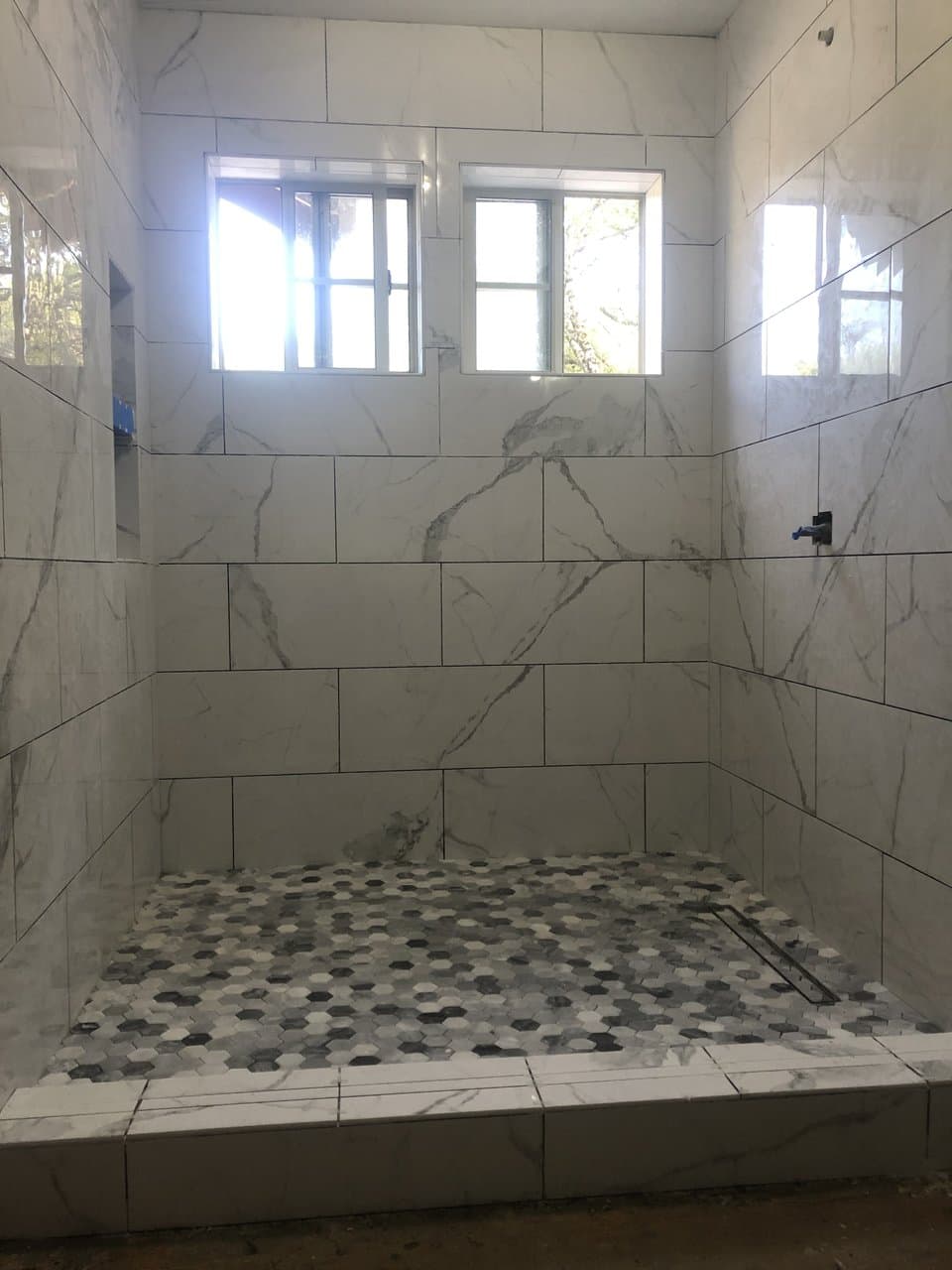 Large marble tile shower with hexagon mosaic floor and linear drain