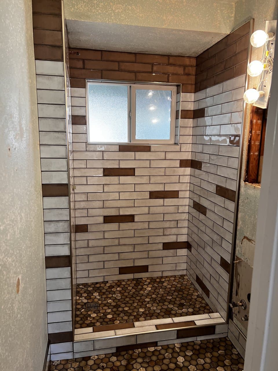 Multi-tone subway tile shower with brown accent tiles and hexagon floor