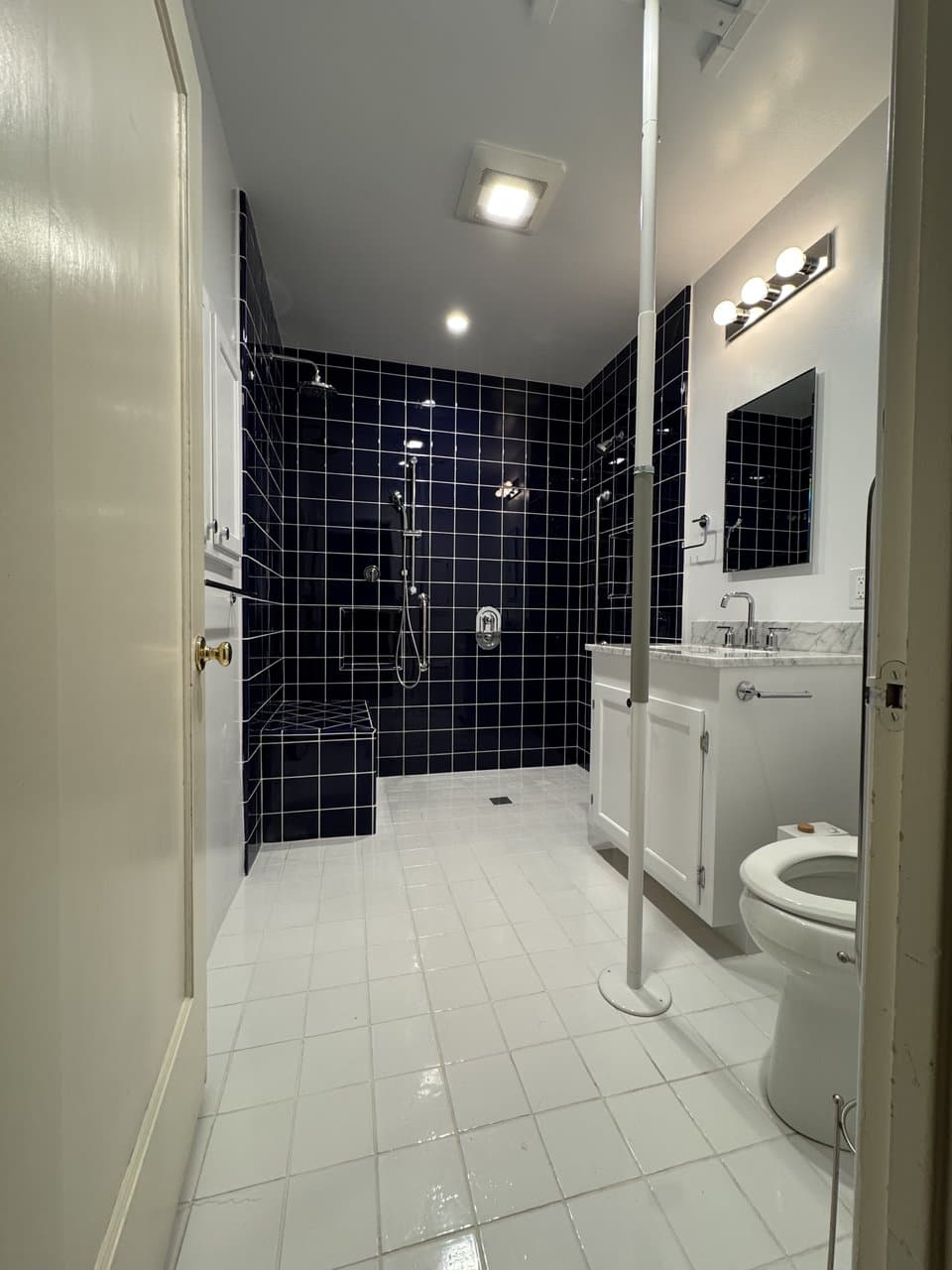 Complete bathroom renovation with navy tile walk-in shower and white tile floor