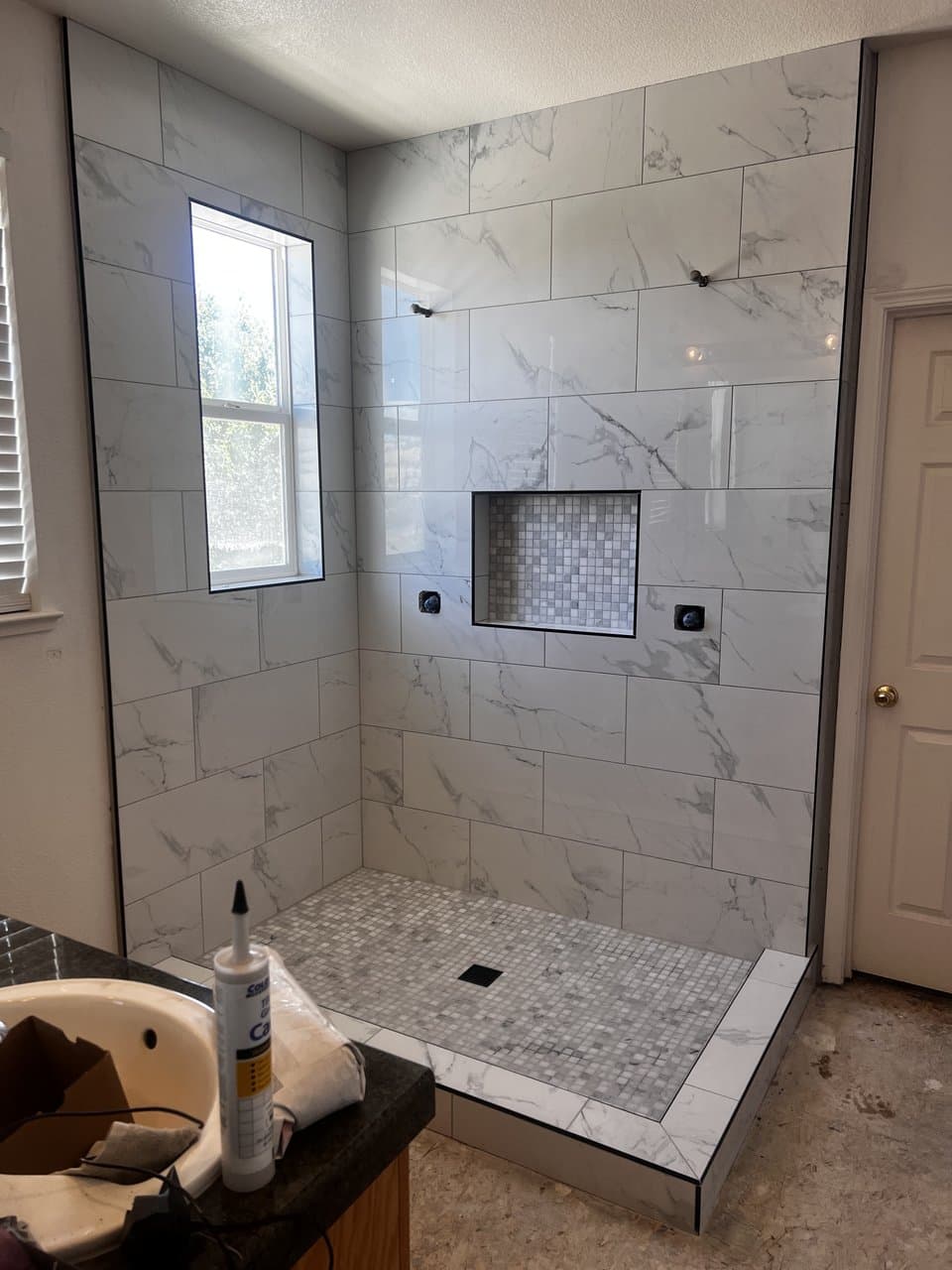White marble tile shower with mosaic niche and floor in progress