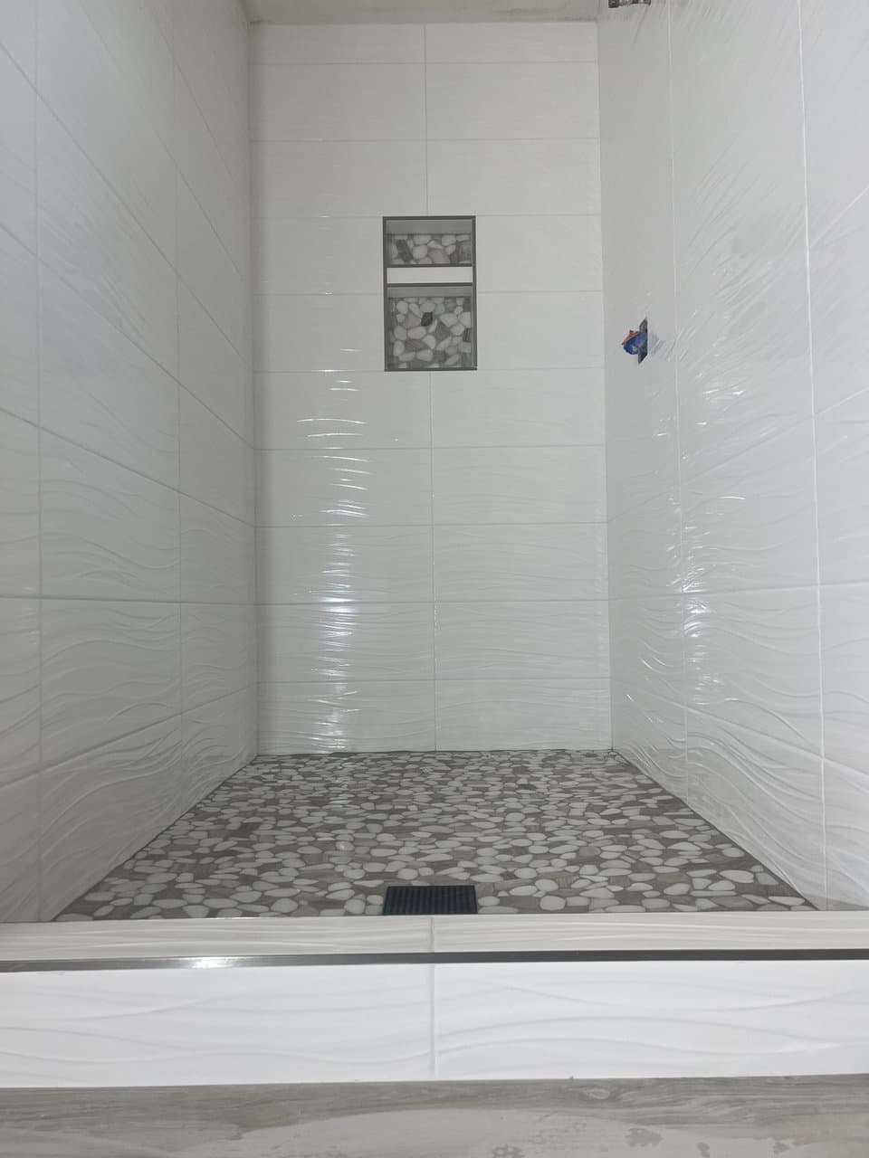 White wave-textured tile shower with pebble stone floor and dual niche